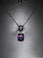 Close-up photo of silver chain necklace with square purple gemstone pendant on black background.
