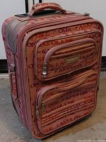 Closed view of the small pink suitcase featuring gasoline themed print and two front pockets with zippers.