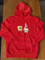Full view of red child's medium hoodie laid flat showing front pocket and character embroidery on chest.