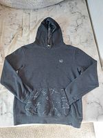 Dark grey Tentree hoodie laid flat on a marble-like surface, showing front side and glow in the dark print on pouch pocket.