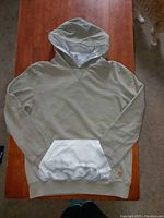 Full front view of olive-green Tentree hoodie with white kangaroo pocket and hood lining, laid flat on wooden surface.