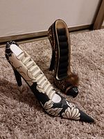 View of two high heel shoe ring holders placed side by side on carpet. Black and white floral shoe on right side, leopard print shoe on left side.