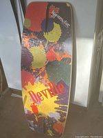 Wakeboard top side showing colorful paint splash pattern and Deville logo.