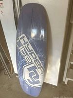 Photo showing bottom side of the wakeboard with large 'Hyperlite' logo, purple nose and tail, and light surface wear.