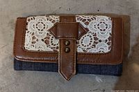 Closed purse showing brown leather with white crochet lace and leather strap detail on front flap.