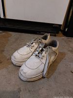 Pair of white worn women's sneakers on concrete floor, showing scratches and signs of wear.