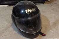 Black full-face motorcycle helmet with 'RAIDER' branding on front, view with visor down.