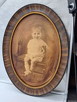 Full view of oval framed portrait showing seated child and wooden frame
