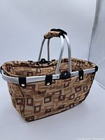 Side view of foldable shopping basket showing geometric pattern and aluminum frame.