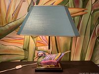 Side view of the ceramic duck lamp with blue shade against a floral mural background.