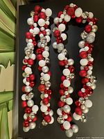 Three long Christmas garlands made from red, white, silver, and glittery spherical ornaments arranged on a dark surface.