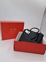 Black Coach leather tote bag placed inside red Coach box with lid. Shows included original packaging.
