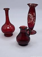 Three cranberry glass vases: tall etched vase, round vase, pitcher vase