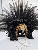 Full view of the decorative black velvet mask with gold ribbon flowers and large black feathers in a fan shape on the top and sides.