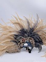 Full side view of the vintage decorative mask featuring large beige and grey feathers, seashells, starfish, lace, pearls, and a small mirror.