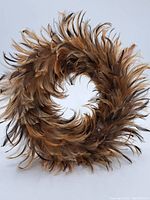 Full view of the circular feather wall hanging showing its overall size and shape with layered brown and tan feathers.