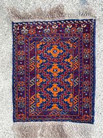 Full view of the rug laid flat showing the geometric central pattern in orange and blue with floral borders and fringes.