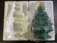 The original Styrofoam packaging and the ceramic Christmas tree inside a plastic bag, showing the shape and packing condition.
