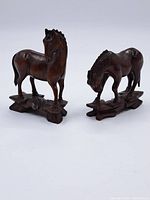 Two carved wooden horses, one with head turned, the other grazing on wooden bases.