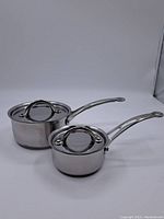 Two Jamie Oliver stainless steel saucepans with lids, varying sizes, shown against a white background.