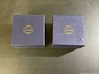 Two closed navy blue boxes with gold Sorelle logo on the lid showing branding and packaging of the ornaments