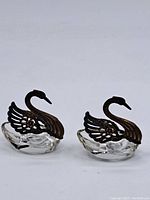 Lot of two swan ornaments side by side showing metal wings and clear glass bases.