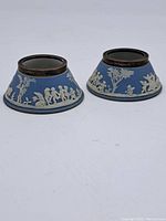 Pair of conical Wedgwood ink wells showing blue jasperware bodies with classical white relief decorations and metal rims.