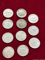 Eleven Canadian silver quarters arranged on red fabric showing the cougar design and date 1867-1967, visible tarnish and wear.