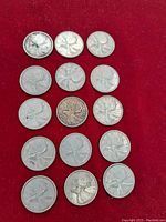 Fourteen Canadian silver quarters arranged on a red surface, showing general wear and tarnish.