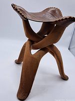 Full view of the carved wooden folding stool showing the interlocking curved legs and leather seat.