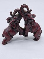 Front view showing two red resin elephants standing side by side with intertwined trunks.