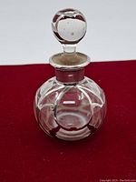 Front view of vintage round glass perfume bottle with sterling silver overlay and round glass stopper showing wear and chip on stopper base.
