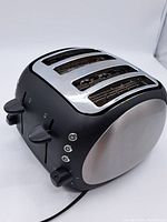 Front angle of toaster showing four slots with stainless steel cover and black plastic body with two levers and dials.