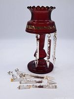 Full view of cranberry glass candle holder with some crystal prisms hanging and others detached on the surface below