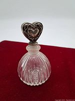 Angled front view of the ribbed glass perfume bottle with heart-shaped silver-tone stopper