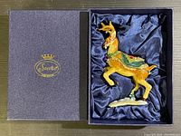 Top-down photo showing reindeer ornament in open black box lined with dark blue satin fabric, with gold Sorelle logo on box lid.