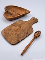 Full view of leaf-shaped wooden bowl, cutting board, and honey dipper shown on white background.