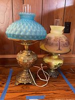 Pair of ornate hurricane lamps on wooden surface, showing full bodies and shades