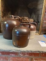 Three stoneware jugs placed on fireplace hearth, showing size and coloration with one two-tone jug and two fully dark brown jugs.