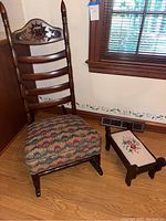 Full view of antique rocker with carved sun and cloth seat, alongside the embroidered footstool to the right.