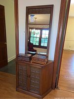 Wooden cabinet with carved two-door front panel with two wooden jewelry boxes on top and large matching mirror behind attached to the wall.