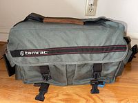 Closed gray Tamrac camera bag with logo, sitting on wood surface