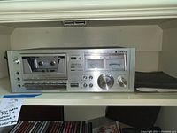 Front view of Sanyo cassette deck showing cassette compartment, control buttons, VU meters, and knobs.