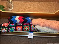 Four handmade afghans folded and placed on a shelf, showing colors and crochet detail.