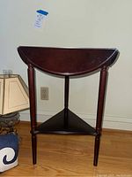 Front view of the solid dark wood end table showing closed drop leaves and three legs.