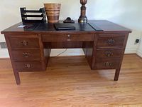 Front view of the vintage wooden desk with three drawers on each side and leather inlay on the desk surface.