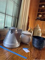 Photo showing large aluminum Wear-Ever coffee pot, ceramic vessel, and cast iron cauldron on wood table near window with natural light.