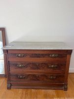 Front view of vintage wooden dresser with removable white marble top and attached mirror leaning against wall.