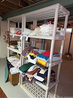 View of two beige plastic shelving units with folded linens stacked on shelves in basement.