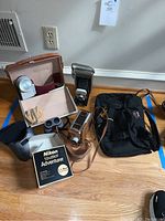 Full overview of cameras, binoculars, straps and bag arranged on floor
